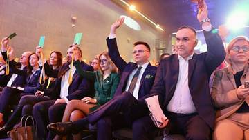 Ludzie siedzący w rzędach, niekt&oacute;rzy z podniesionymi rękami.