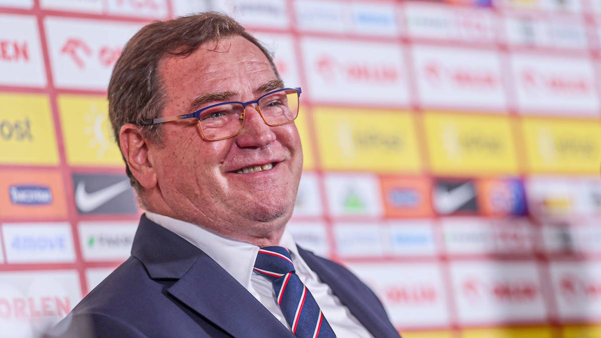 Portret Jana Urbana, trenera reprezentacji Polski, siedzącego na tle ścianki z logotypami sponsorów.