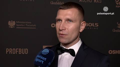 Tomasz Dylak w garniturze i muszce udziela wywiadu, z widocznymi logotypami sponsor&oacute;w w tle.