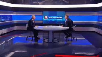 Dw&oacute;ch mężczyzn w garniturach siedzi przy okrągłym stole w studiu telewizyjnym.