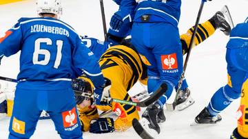 Hokeiści walczą o krążek na lodowisku, jeden z zawodnik&oacute;w leży na lodzie.