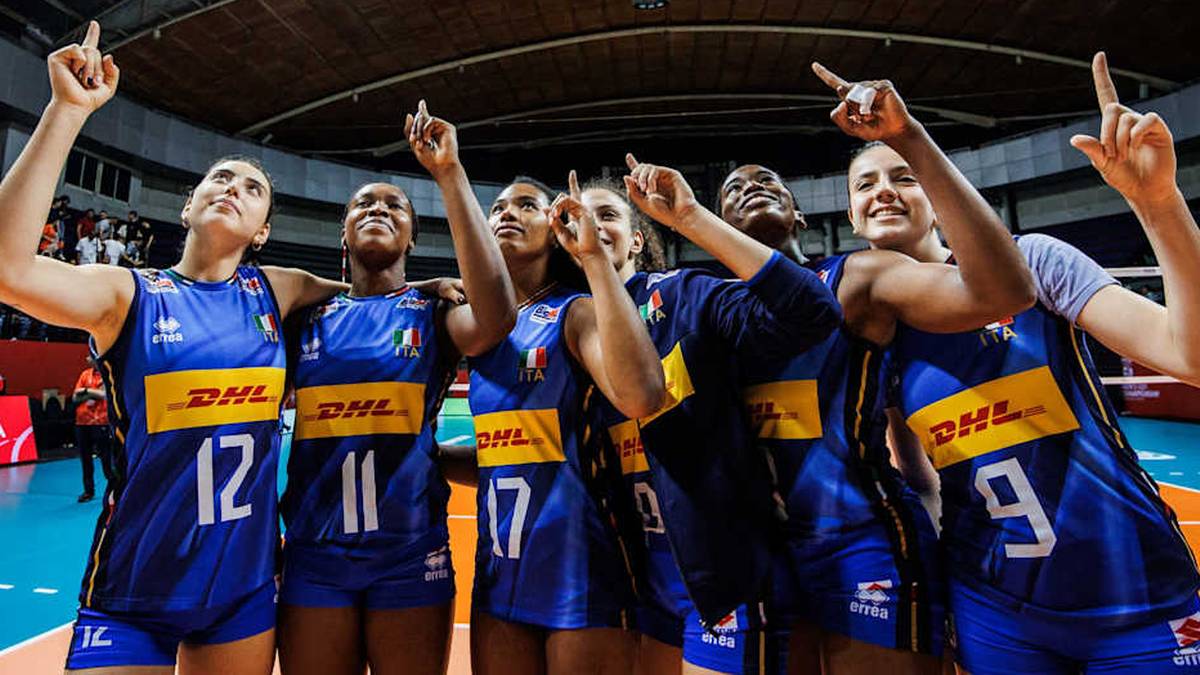 Sześć siatkarek w niebieskich strojach z żółtymi napisami i numerami na plecach, stojących obok siebie i wskazujących palcami w górę, patrzących w stronę obiektywu.