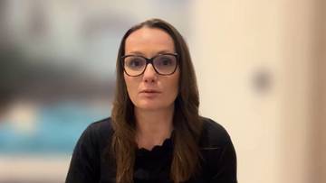 Portret kobiety noszącej okulary w czarnych oprawkach, z brązowymi włosami i czarnym ubraniem.