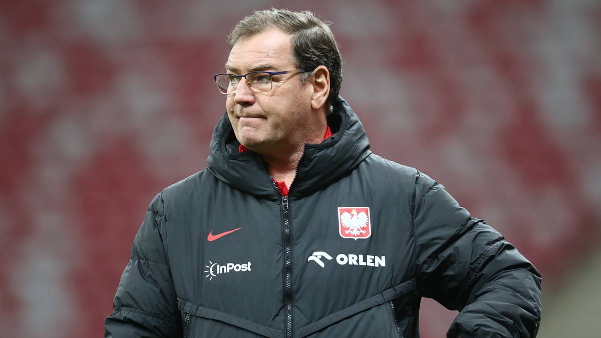 Trener reprezentacji Polski w kurtce z godłem Polski, stojący na boisku