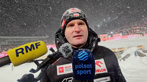 Mężczyzna w czapce i kurtce zimowej z mikrofonami RMF i Polsat Sport na tle śniegu i trybun.