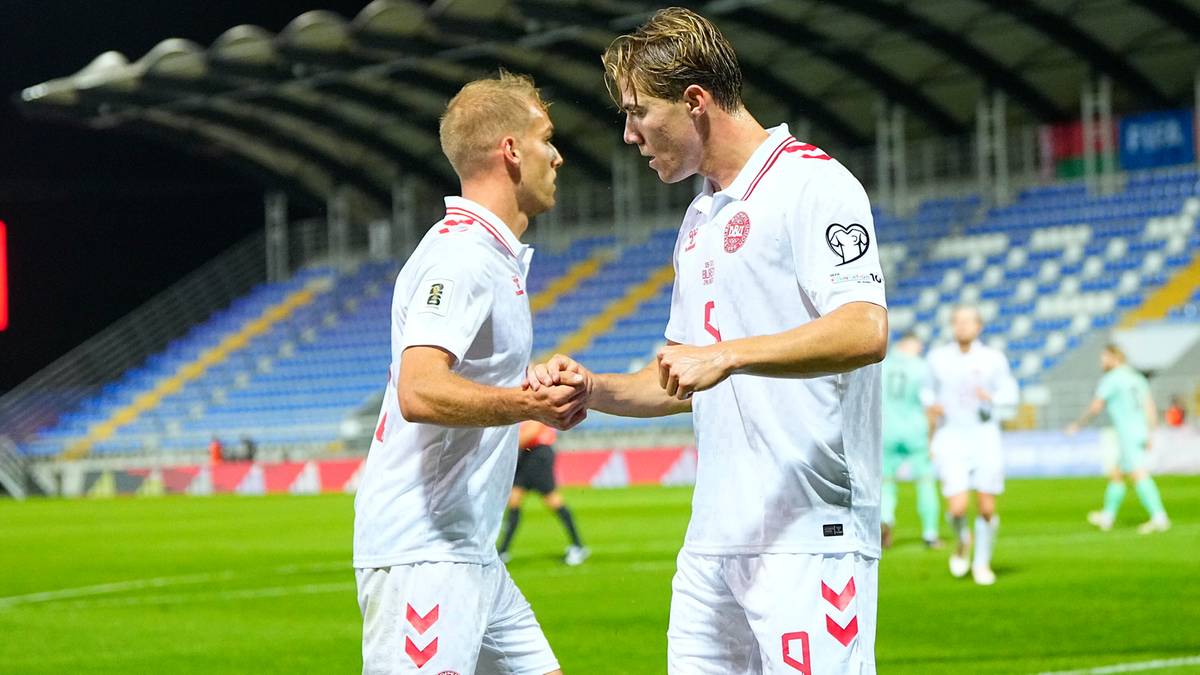 Dw&oacute;ch piłkarzy Danii w białych koszulkach uściskuje sobie dłonie na boisku piłkarskim.