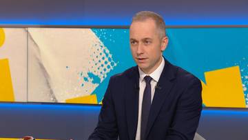 Mężczyzna w garniturze i krawacie wypowiadający się w studio telewizyjnym