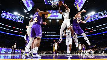 Koszykarze w akcji podczas meczu, jeden zawodnik wyskakuje do wsadu, inny próbuje go zablokować. Na drugim planie widać kibiców i parkiet.