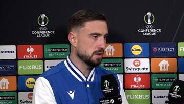 Filip Jagiełło udziela wywiadu przed ścianką sponsorską Ligi Konferencji Europy.