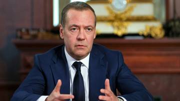 Dmitrij Miedwiediew w granatowym garniturze i białej koszuli z krawatem, siedzący przy stole.