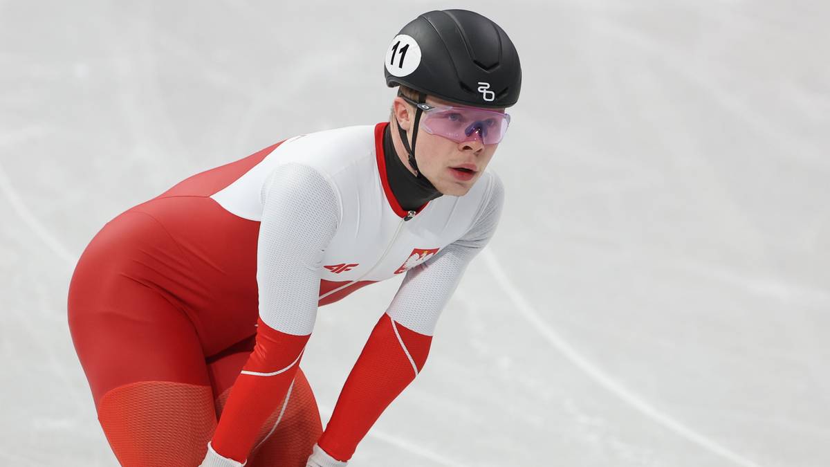 Michał Niewiński w stroju łyżwiarskim pochyla się na lodzie.