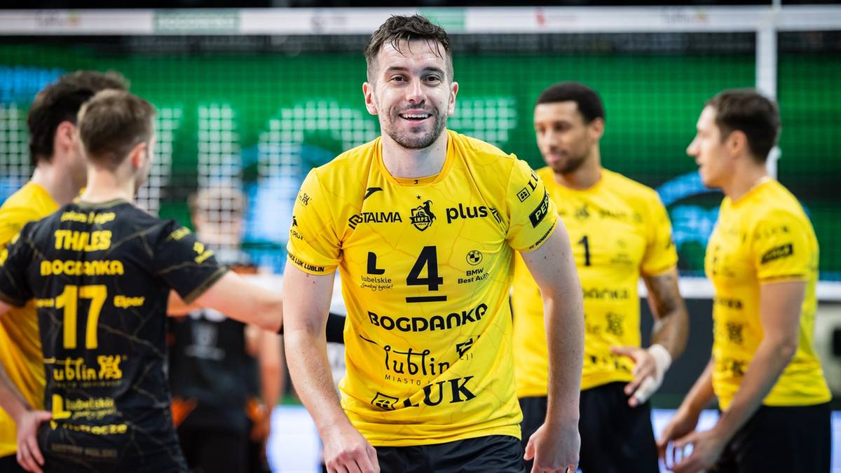 Siatkarz w żółtej koszulce z numerem 4 na piersi uśmiecha się, otoczony przez kolegów z drużyny na boisku.