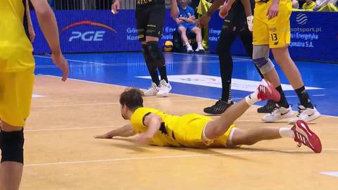 Siatkarz w ż&oacute;łtej koszulce leży na parkiecie, pr&oacute;bując obronić piłkę.