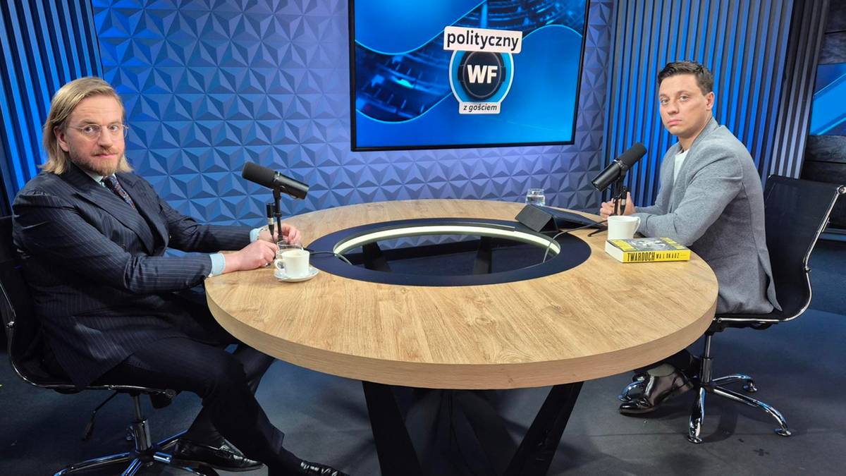 Dwóch mężczyzn siedzi przy okrągłym stole w studiu telewizyjnym na tle niebieskiej dekoracji ściennej z logo Polityczny WF.