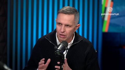 Roman Kołtoń, dziennikarz sportowy, wypowiada się do mikrofonu na tle studia telewizyjnego.