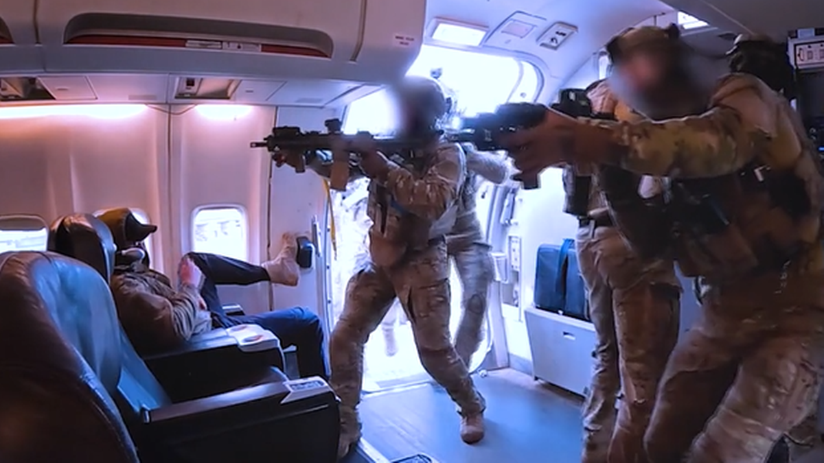 Członkowie JW GROM w pełnym umundurowaniu, z bronią w rękach, wykonują symulację odbicia samolotu pasażerskiego. Wchodzą do kabiny, celując.