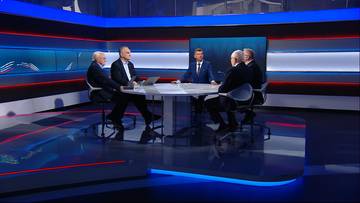 Czterech mężczyzn siedzi przy okrągłym stole w studiu telewizyjnym, rozmawiając.