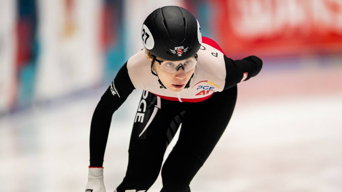 Kobieta w kasku i okularach ochronnych jedzie na łyżwach po lodzie, ubrana w kombinezon sportowy z numerem 27.