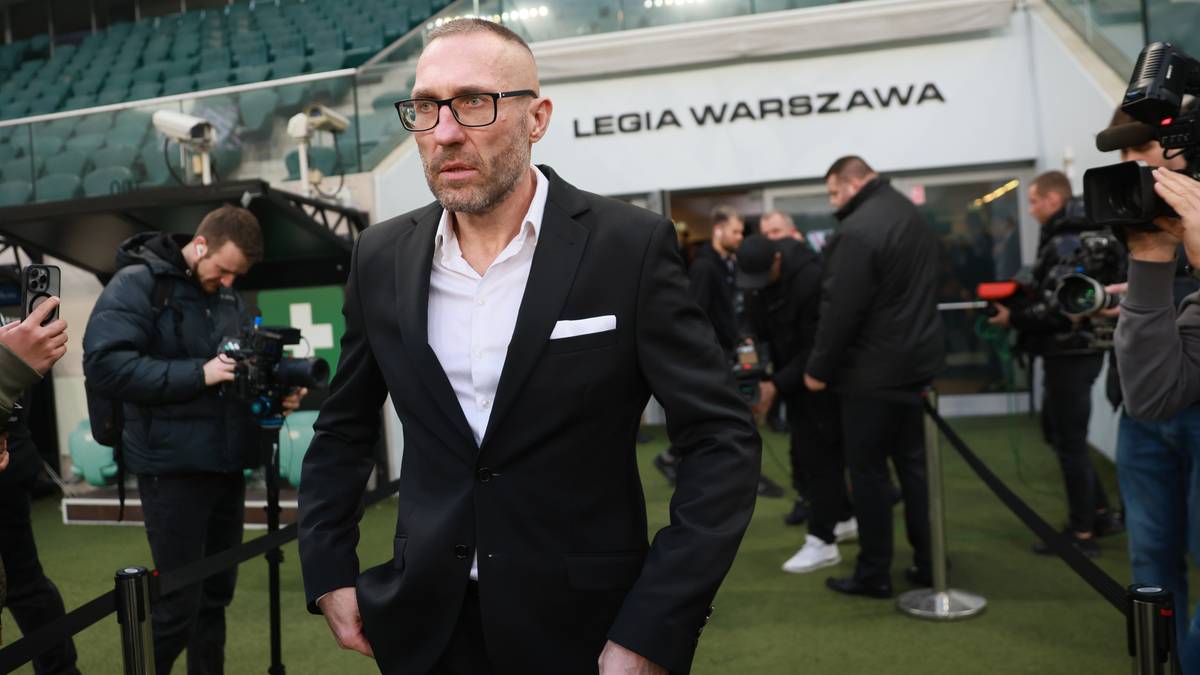 Marek Surowiec, nowy dyrektor sportowy Legii Warszawa, w garniturze i okularach, wychodzi na boisko stadionu.
