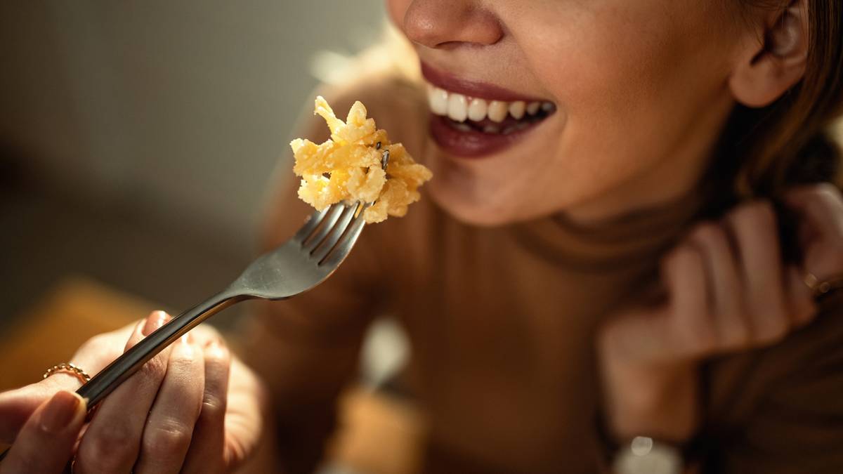 Uśmiechnięta kobieta jedząca widelec z makaronem.