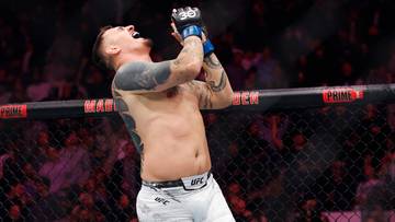 Zawodnik MMA w rękawicach i spodenkach UFC unosi ręce w geście triumfu, krzycząc