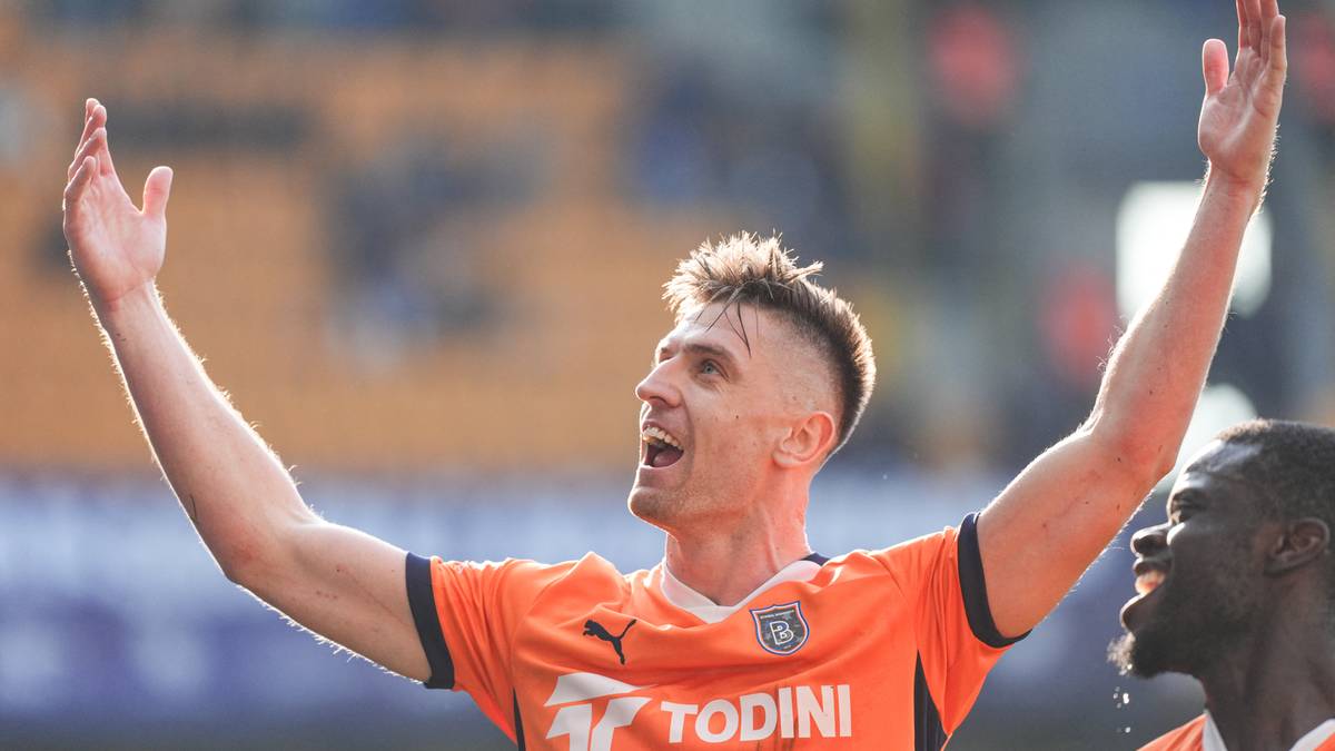 Piłkarz w pomarańczowej koszulce świętuje zwycięstwo, wznosząc ręce do góry.