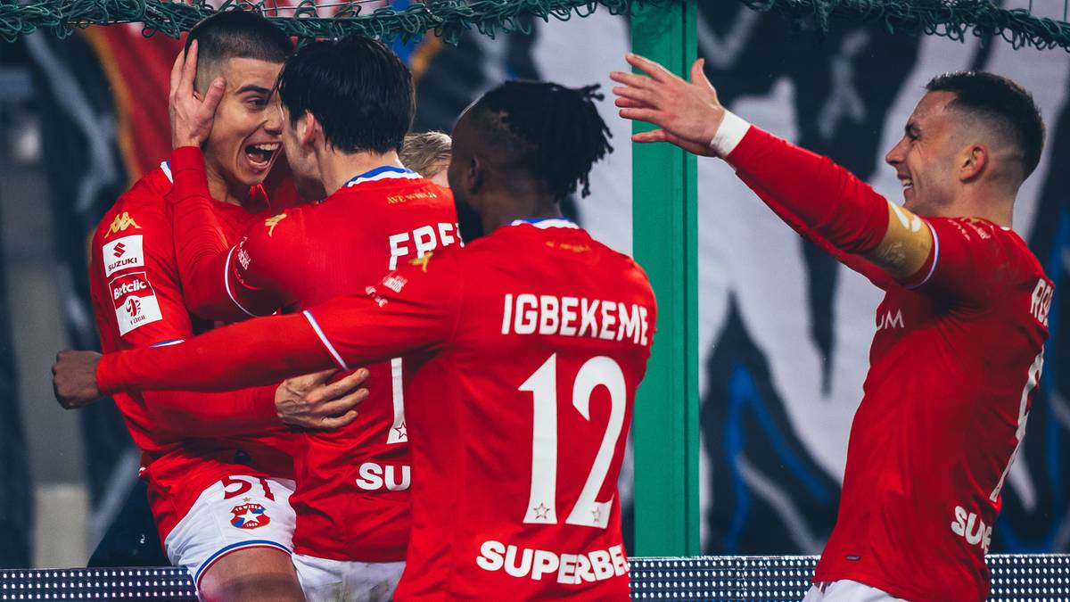 Grupa piłkarzy w czerwonych strojach świętuje radośnie zdobycie bramki na boisku.