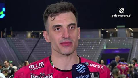 Zbliżenie na twarz siatkarza Wassima Ben Tary, ubranego w czerwoną koszulkę z widocznymi logotypami sponsor&oacute;w, w tle trybuny stadionu.