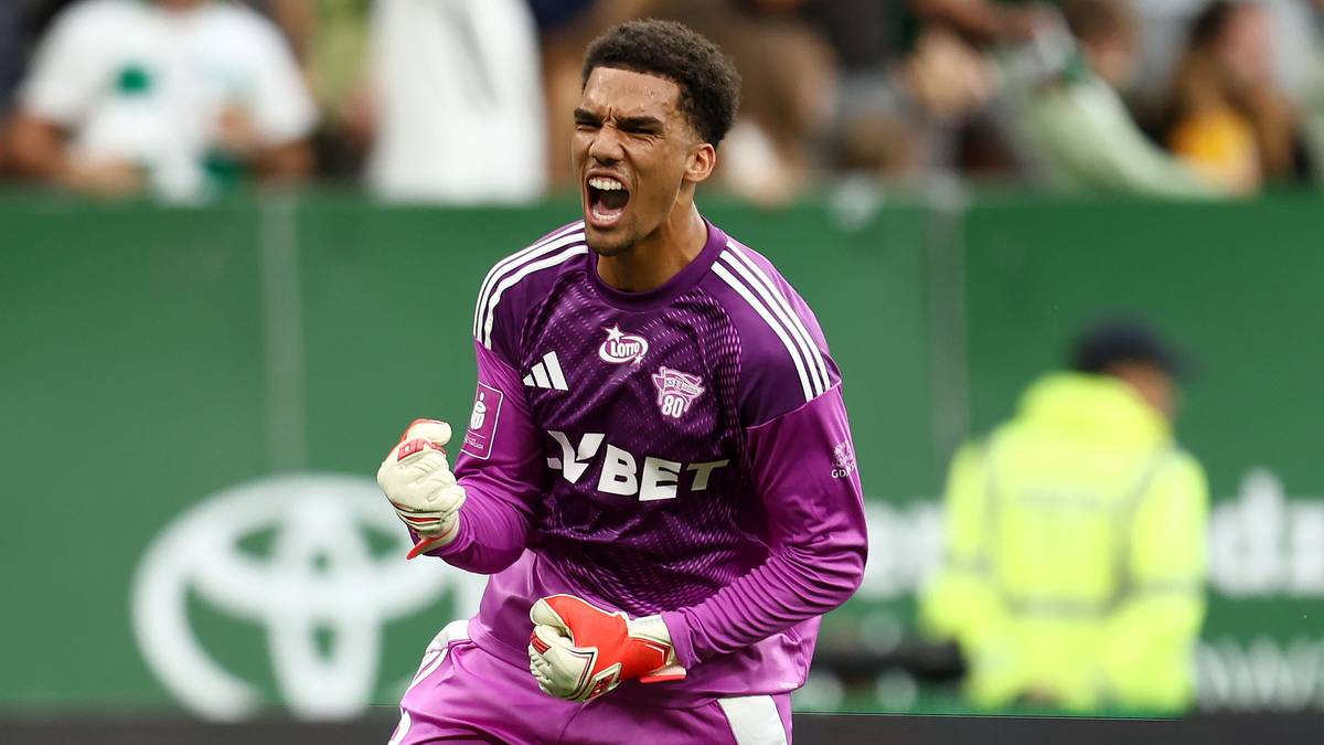 Bramkarz Lechia Gdańsk w stroju fioletowym i białych rękawicach, krzyczy z zaciśniętą prawą pięścią uniesioną do góry.