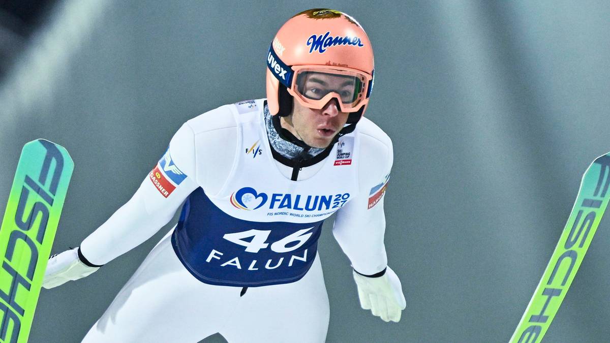 Skoczek narciarski w białym kombinezonie z numerem 46 na piersi, w pomarańczowym kasku i goglach, gotowy do skoku.