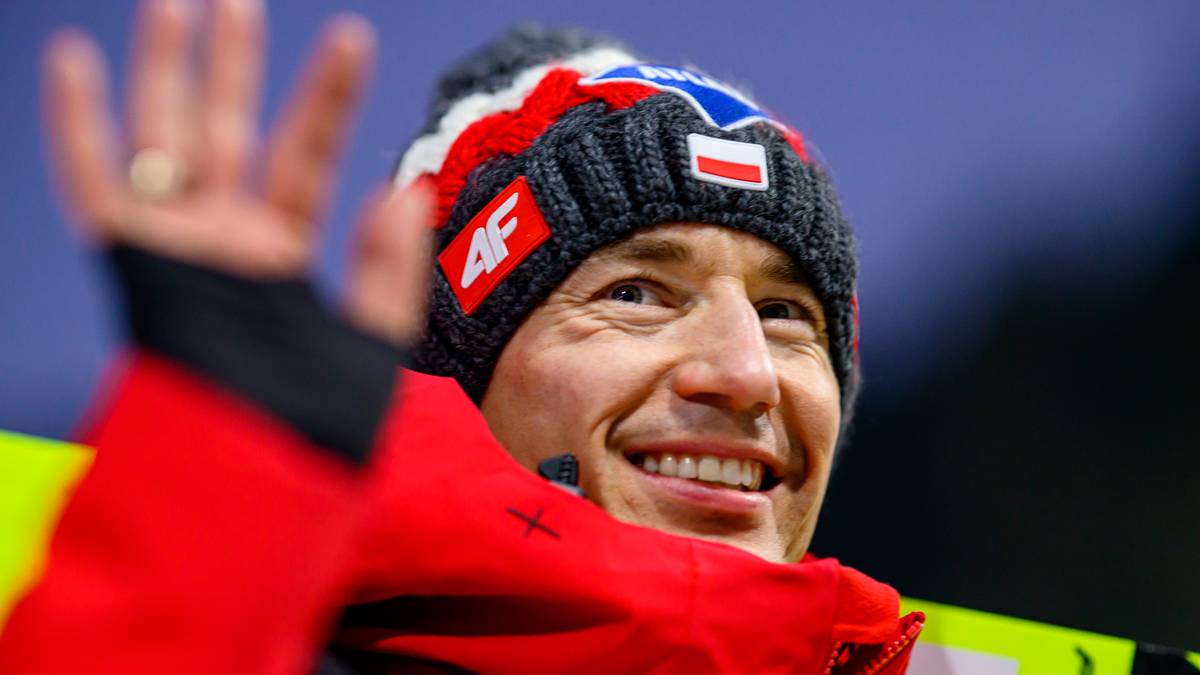 Portret Kamila Stocha, uśmiechniętego polskiego skoczka narciarskiego, w czapce zimowej z polskimi barwami i logo marki odzieży sportowej.