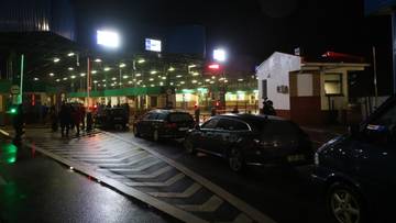 Nocny widok na oświetlony punkt kontrolny na granicy, z kolejką samochodów i budynkami straży granicznej.