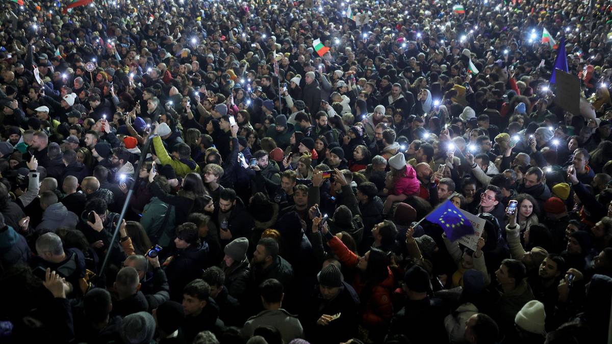 Tłum ludzi trzymających zapalone telefony komórkowe podczas protestu nocą.