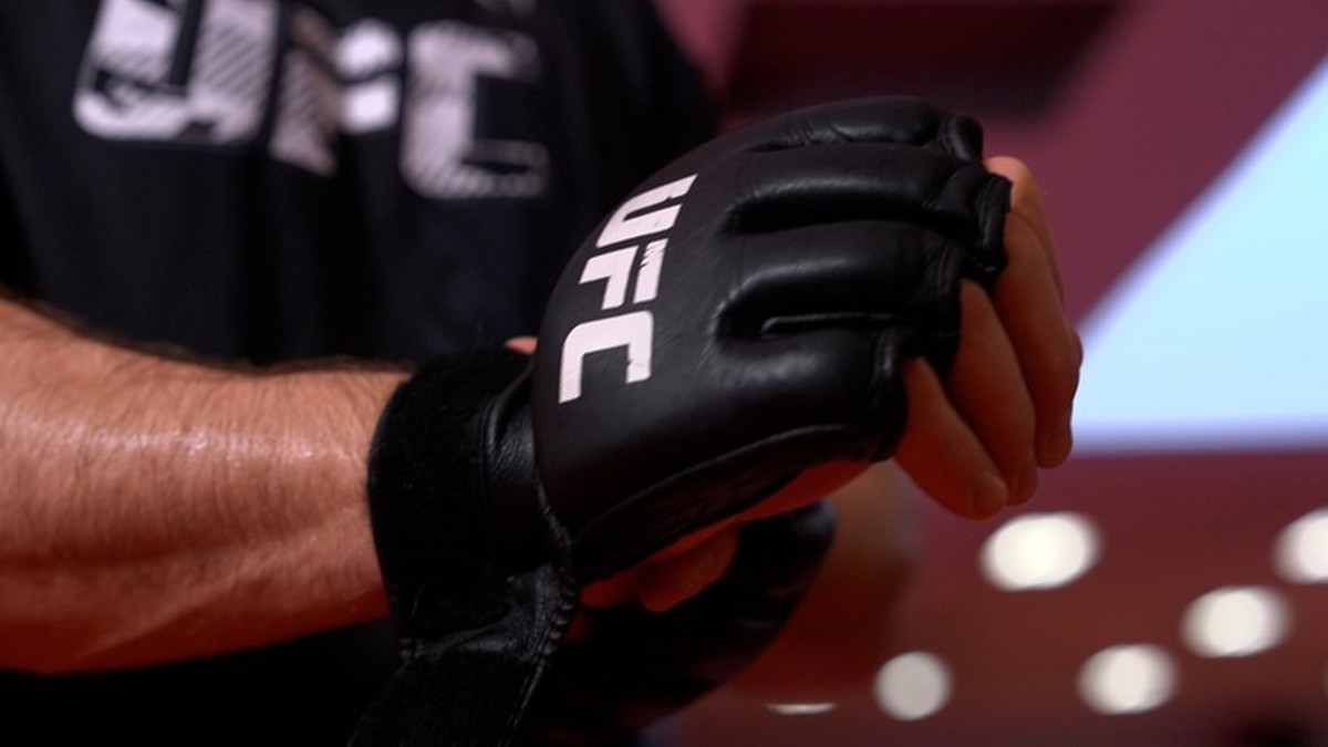 Zbliżenie na dłoń zawodnika UFC zakładającego czarną rękawicę z białym logo UFC.