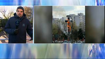 Płonący krzyż na tle budynk&oacute;w mieszkalnych i nieba.