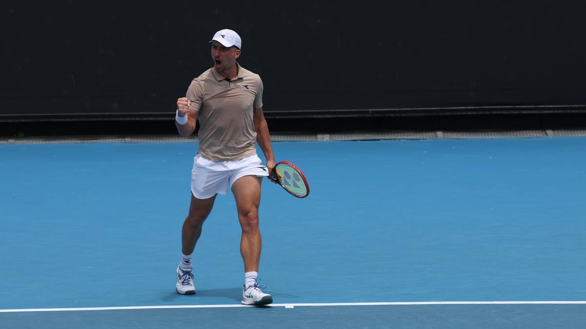 Mężczyzna grający w tenisa, trzymający rakietę i gestykulujący ręką w geście zwycięstwa.