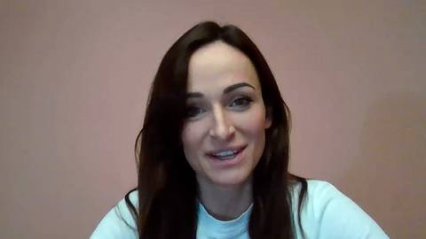 Portret Iwony Januszyk, kobiety z długimi brązowymi włosami, uśmiechającej się do kamery. Ma na sobie białą bluzkę.