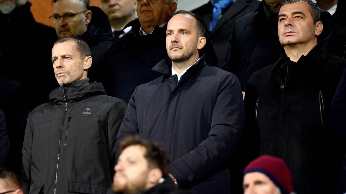 Trzech mężczyzn w ciemnych kurtkach, patrzących w kierunku widza. Mężczyzna po lewej ma kr&oacute;tko przycięte, siwe włosy i jest lekko pochylony. Mężczyzna w środku ma zarost i ciemne włosy, ubrany jest w ciemną kurtkę. Mężczyzna po prawej ma kr&oacute;tkie, czarne włosy i patrzy prosto przed siebie.