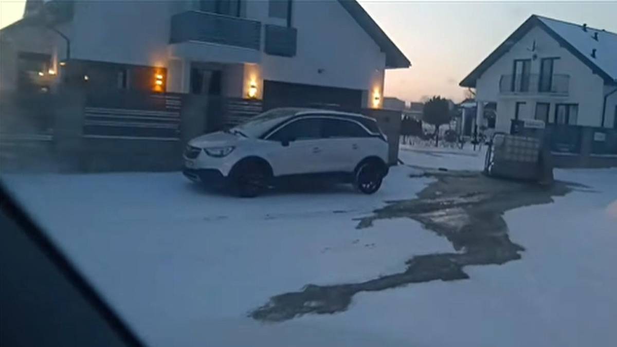 Biały samoch&oacute;d zaparkowany przed domem na ośnieżonej drodze.