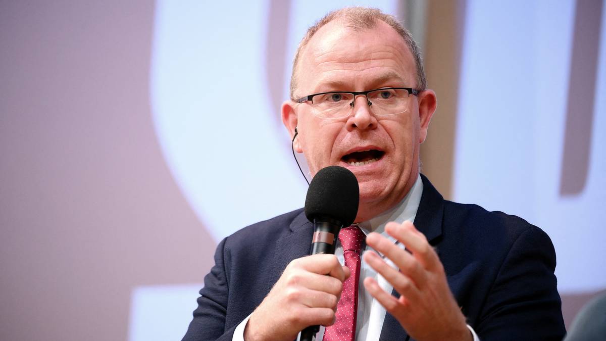 Mężczyzna w okularach i garniturze przed mikrofonem, aktywnie gestykulujący.