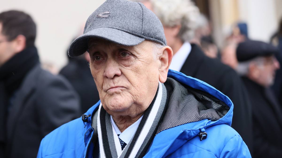 Portret starszego mężczyzny w szarej czapce i niebieskiej kurtce.