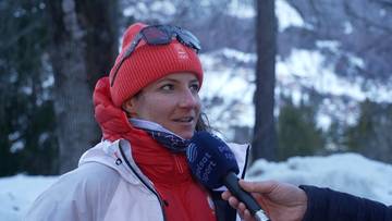 Maryna Gąsienica-Daniel w czerwonej czapce i goglach narciarskich udziela wywiadu na tle zimowego krajobrazu.