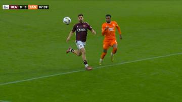 Dwóch piłkarzy na zielonym boisku podczas meczu piłki nożnej, jeden w bordowej koszulce z logo Heart of Midlothian FC, drugi w pomarańczowej koszulce Rangers FC.