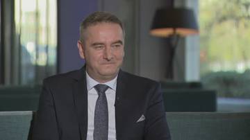 Mężczyzna w garniturze z krawatem siedzi w pomieszczeniu, jego twarz skierowana lekko w prawo.