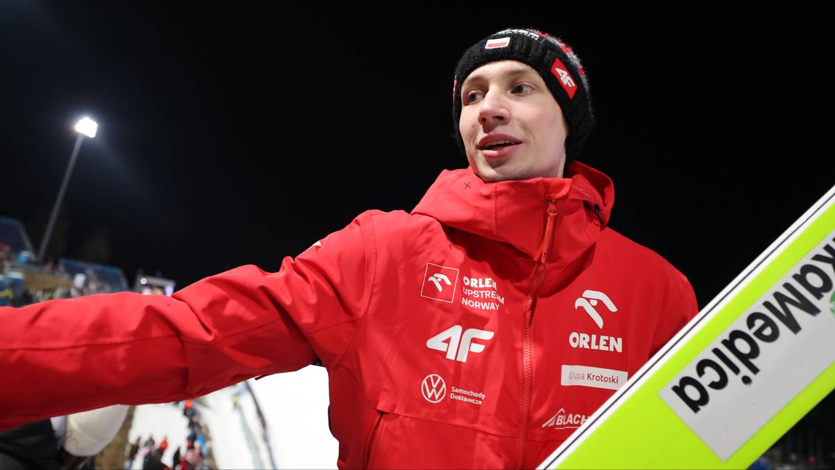 Mężczyzna w czerwonej kurtce narciarskiej z czarną czapką z czerwonymi i białymi wzorami.