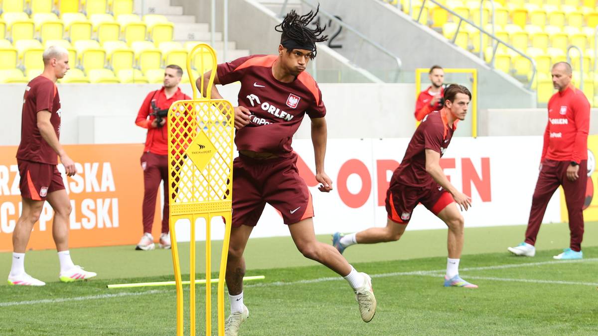 Piłkarz w bordowej koszulce reprezentacji Polski wykonuje ćwiczenie z żółtym pachołkiem.
