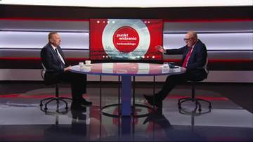 Dwóch mężczyzn w garniturach siedzi przy stole w studiu telewizyjnym, rozmawiając na tle ekranu z logo programu "Punkt widzenia".