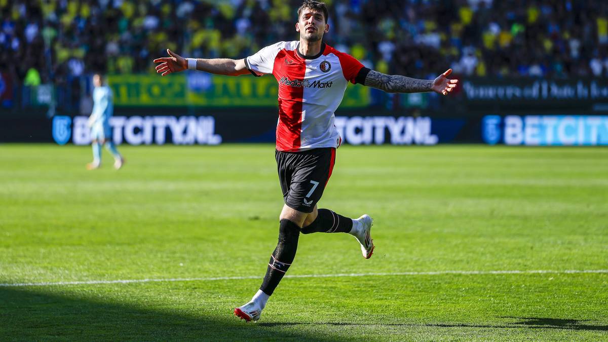 Piłkarz w koszulce Feyenoordu biegnie po boisku z uniesionymi rękami.