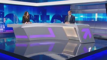 Dwoje prezenter&oacute;w siedzi przy futurystycznym stole w studiu telewizyjnym z niebieskim podświetleniem.