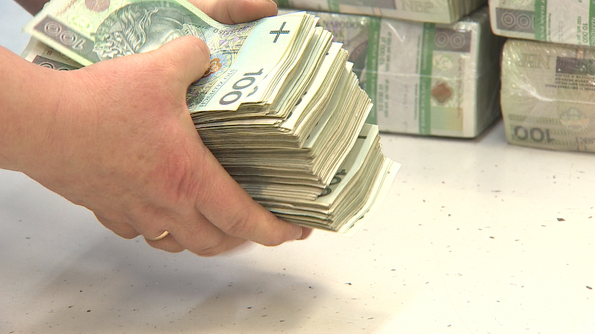 Dłonie trzymające dużą stertę banknotów 100-złotowych.
